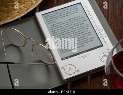 Sony e-Reader 2008 , première génération un livre numérique portable électronique dispositif de stockage et de lecture sur une table avec chapeau de paille et lunettes Banque D'Images