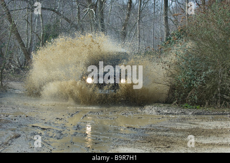 Une Land Rover Defender 90 touches par une piste inondée à woodland dans Sutton West Sussex UK au cours d'un exercice hors route. Banque D'Images