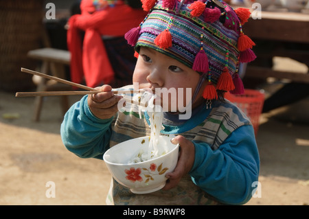 Garçon Hmong farce son visage avec des nouilles au cours du marché à Tam Duong près de Sapa Vietnam Banque D'Images