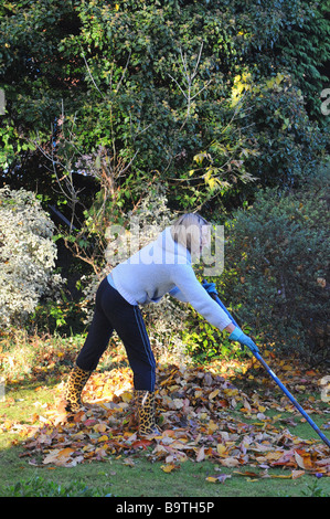 Femme blonde ramasser des feuilles dans son jardin Banque D'Images