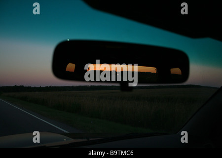Lune passant par la fenêtre avant et le coucher de soleil dans le rétroviseur tout en conduisant Banque D'Images