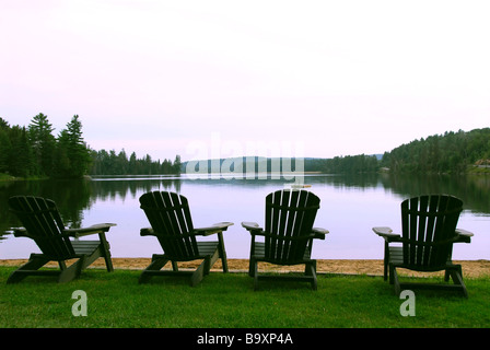 Quatre chaises Adirondack en bois sur un rivage d'un beau lac au crépuscule Banque D'Images