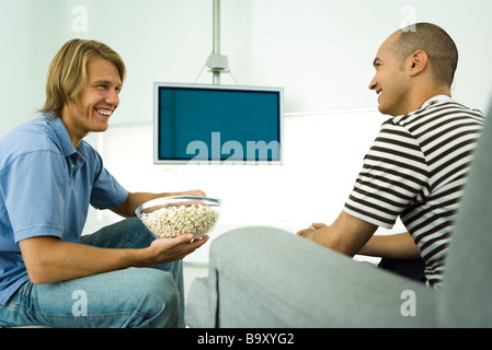 Deux hommes discutant et eating popcorn, télévision écran plat en arrière-plan Banque D'Images