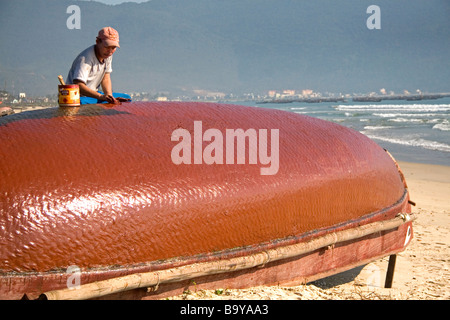 Pêcheur vietnamien en imperméabilisant les fond d'un bateau en fibres tissées sur la Chine plage près de la ville portuaire de Da Nang Vietnam Banque D'Images