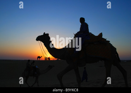 Les touristes et de chameaux sur les dunes de sable de Jaisalmer, tandis que le soleil se couche sur l'horizon. L'État du Rajasthan, en Inde. Banque D'Images