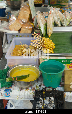 Gros plan de sauce satay et de bâtonnets de poulet satay prêts à être grillés sur un stand de Bangkok Banque D'Images