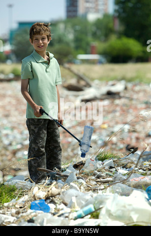 Boy picking up bouteille en plastique en décharge, smiling at camera Banque D'Images