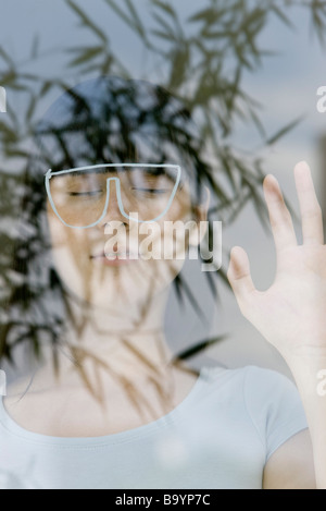 Jeune femme avec les yeux fermés, derrière l'élaboration de lunettes, vu à travers la réflexion de plante Banque D'Images