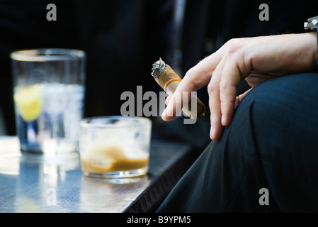 La main de l'homme sur la tenue du genou fumeurs de cigare, close-up Banque D'Images