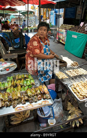 Une femme faisant de bananes grillées brochettes et colis sur son étal de Bangkok Banque D'Images