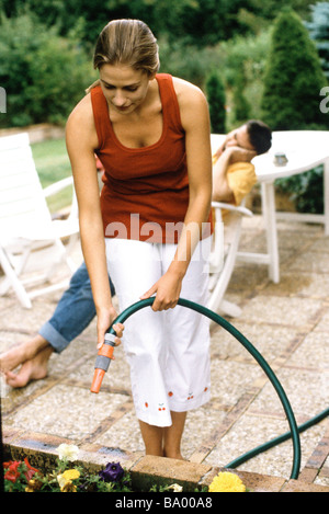 Woman watering flowers avec tuyau de jardin, l'homme allongé en arrière-plan Banque D'Images