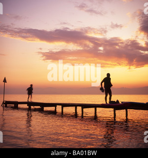 Les gens se silhouettaient au coucher du soleil sur une jetée en bois au-dessus d'un lac. Lac de Garde, Italie Banque D'Images