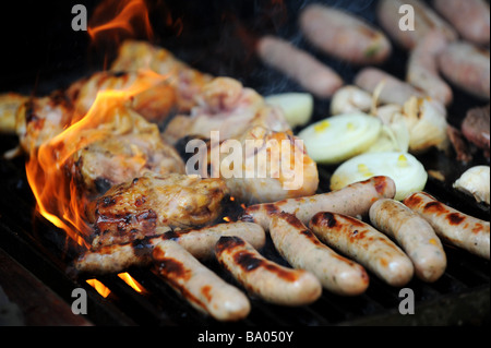 Les flammes lèchent tour beefburgers, saucisses, poulet et faire cuire sur un barbecue à gaz Banque D'Images