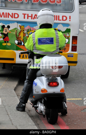 London Metropolitan police Community support Officer sur Motor scooter enregistrant les détails de la camionnette à glace sur les lignes rouges doubles Angleterre Royaume-Uni Banque D'Images