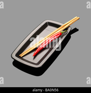 Piments rouges frais sur une plaque avec chopstikcs sur gray reflective surface Banque D'Images
