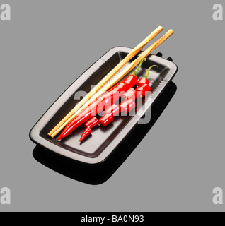 Piments rouges frais sur une plaque avec chopstikcs sur gray reflective surface Banque D'Images
