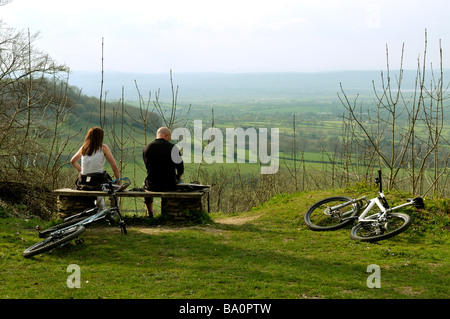 Les cyclistes reste sur banc avec vue sur vallée de la Severn de Cotswold Hills au printemps en Angleterre Banque D'Images