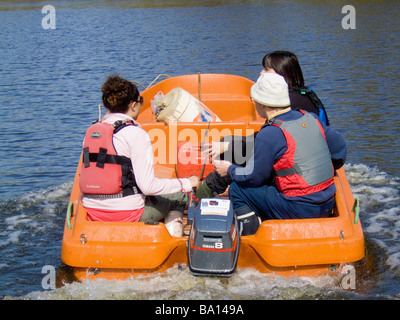 Vue arrière de 3 personnes en bateau de moteur avec la femme helms portant une corde de tuer, sur la rivière Ouse à York. Banque D'Images