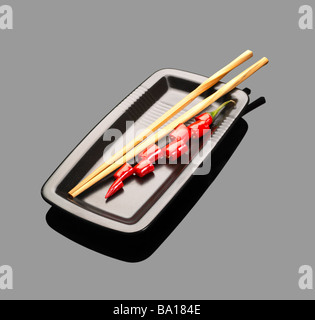 Piments rouges frais sur une plaque avec chopstikcs sur gray reflective surface Banque D'Images