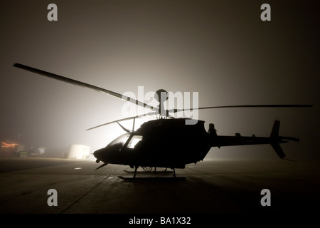 L'illumination du voyant lumineux silhouettes un OH-58D Kiowa hélicoptère pendant un épais brouillard. Banque D'Images