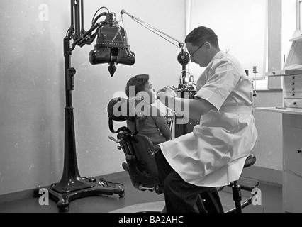 Clinique dentaire, 1950s. Un jeune garçon assis dans une chaise, les dents étant vérifiées par un dentiste mâle. Banque D'Images