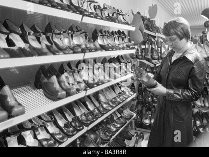 Années 70, photo en noir et blanc, de l'économie, le commerce de détail, jeune femme dans un magasin de chaussures, des étagères avec des chaussures, âgés de 20 à 25 ans, Monika Banque D'Images