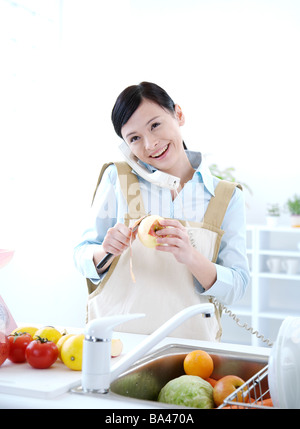 Jeune femme parlant au téléphone dans la cuisine peeling apple smiling Banque D'Images