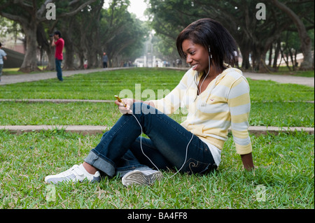 Jeune femme assis dans un parc à l'écoute de la musique sur un lecteur mp3 Banque D'Images