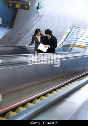 Businessman and businesswoman standing on escalator elevated view Banque D'Images