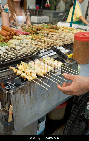 Un gros plan de boulettes de viande grillées et de brochettes de calmar sur un grill de rue de Bangkok Banque D'Images