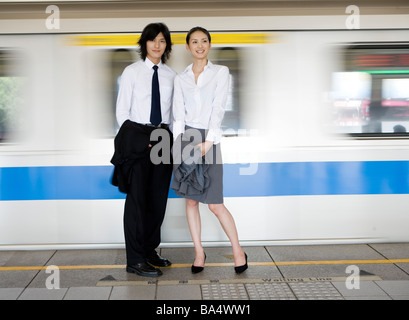 Businessman and businesswoman standing on train platform train passant par blurred motion Banque D'Images