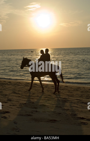 Couple à cheval sur la plage au coucher du soleil à Batu Ferringhi, Penang, Malaisie Banque D'Images