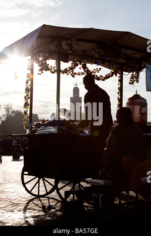 Vendeur jus traditionnels contre le soleil vu de décrochage avec koutoubia minaret en arrière-plan, la place Jemaa el Fna, Marrakech Banque D'Images