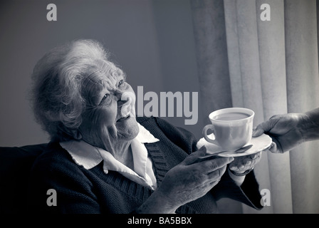 Vieille dame alerte lumineuse heureux de recevoir une tasse de thé d'infirmière soignant compagnon en lumière spacieuse B +W (également en couleur) Banque D'Images