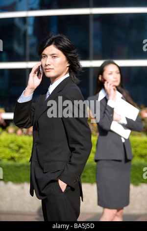 Dans l'avant à l'aide d'affaires téléphone cellulaire businesswoman permanent dans l'arrière-plan Banque D'Images