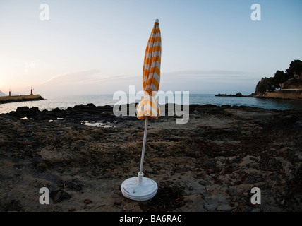 Fermé le jaune et blanc à rayures parasol peuplements dans petite baie sur la côte méditerranéenne espagnole sur tôt le matin Banque D'Images