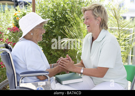 Accueil de la haute direction La haute terrasse gardien rit gaiement en fauteuil roulant les personnes âgées les gens de la série femme 70-80 ans hat chapeau keeper 30-40 Banque D'Images