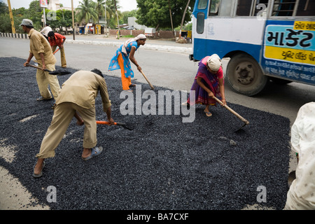 Les travailleurs masculins et féminins / ouvriers répandre sur une route asphaltée à Surat. Le Gujarat. L'Inde. Banque D'Images