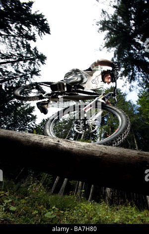 Jeune homme monté sur un VTT sur un tronc, Oberammergau, Bavière, Allemagne Banque D'Images