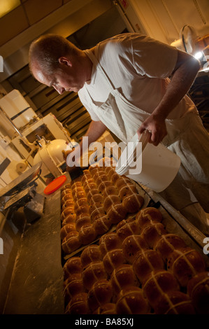 Un boulanger traditionnel rendant les brioches du carême UK - l'application de glacis pour les petits pains cuits au four Banque D'Images