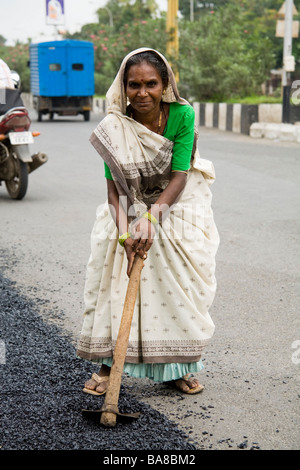 Femme / ouvrier ouvrier répandre sur une route asphaltée à Surat. Le Gujarat. L'Inde. Banque D'Images