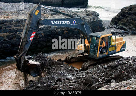 Mechanical digger clearing la rivière sortie de la mer de débris de tempête à Funchal Banque D'Images