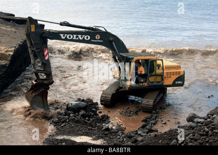 Mechanical digger clearing la rivière sortie de la mer de débris de tempête à Funchal Banque D'Images