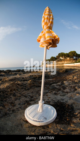 Fermé le jaune et blanc à rayures parasol peuplements dans petite baie sur la côte méditerranéenne espagnole sur tôt le matin Banque D'Images