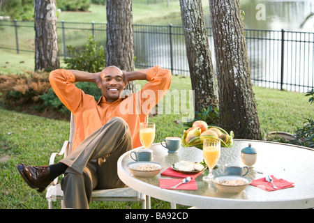 L'homme afro-américain assis à table de petit déjeuner dans le jardin Banque D'Images