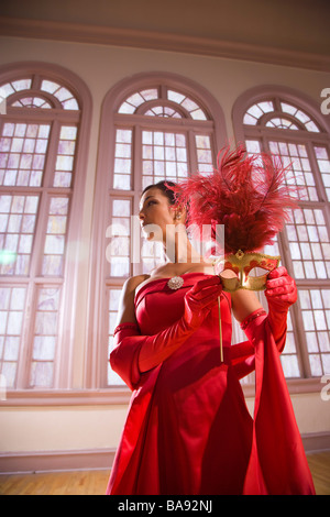 Hispanic woman in robe formelle tenant un masque de bal en permanent Banque D'Images