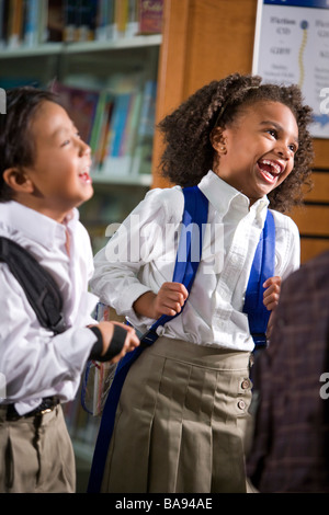 Les Asiatiques et les Africains-Américains les enfants de l'école élémentaire de rire dans la bibliothèque Banque D'Images