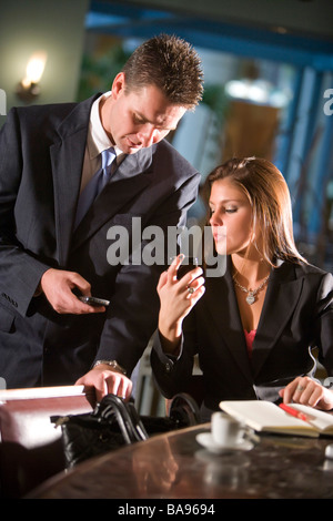Les gens d'affaires dans le restaurant à la recherche à des messages texte sur les téléphones mobiles Banque D'Images