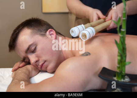 Un jeune mâle adulte reçoit un massage avec bâton de bambou dans un spa Banque D'Images