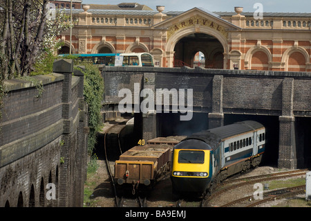 Un train de marchandises passe sous un pont comme un train de voyageurs émerge et un bus est vu sur la route au-dessus Banque D'Images